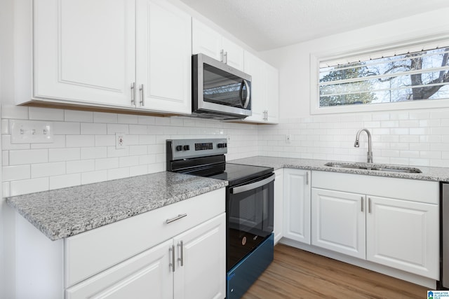 kitchen featuring sink, light stone counters, electric range oven, light hardwood / wood-style floors, and white cabinets