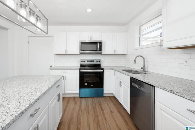 kitchen featuring sink, white cabinetry, stainless steel appliances, light stone counters, and wood-type flooring