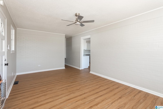 empty room featuring ceiling fan, hardwood / wood-style flooring, a textured ceiling, and brick wall