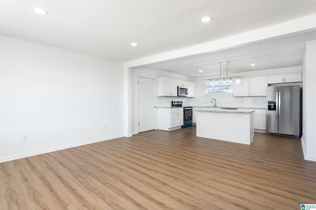 kitchen featuring pendant lighting, light hardwood / wood-style flooring, appliances with stainless steel finishes, a center island, and white cabinets