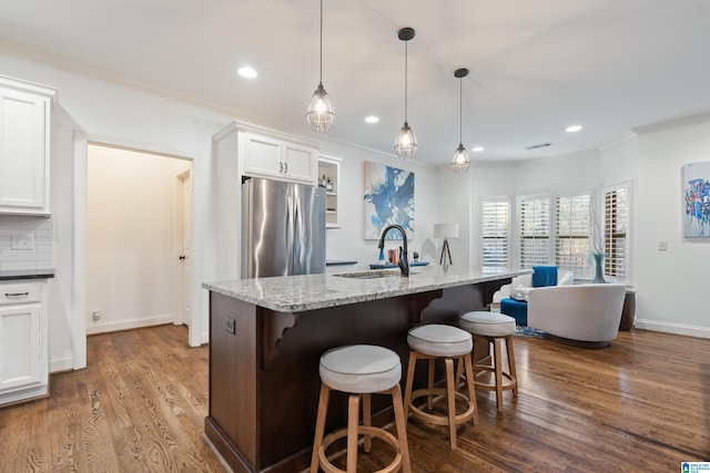 kitchen with sink, white cabinets, stainless steel fridge, hanging light fixtures, and light stone counters