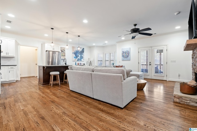 living room with french doors, a stone fireplace, crown molding, hardwood / wood-style flooring, and ceiling fan