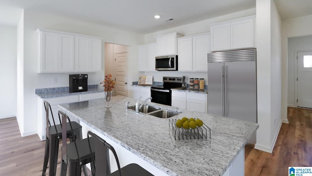 kitchen with white cabinetry, appliances with stainless steel finishes, sink, and a center island with sink