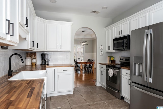 kitchen featuring appliances with stainless steel finishes, decorative light fixtures, butcher block counters, white cabinets, and dark tile patterned floors