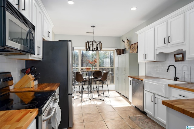 kitchen with decorative light fixtures, white cabinetry, butcher block counters, sink, and stainless steel appliances