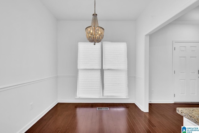 unfurnished dining area featuring an inviting chandelier and dark hardwood / wood-style flooring