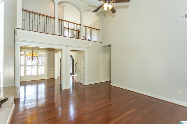 unfurnished living room with ceiling fan with notable chandelier, dark wood-type flooring, and a high ceiling