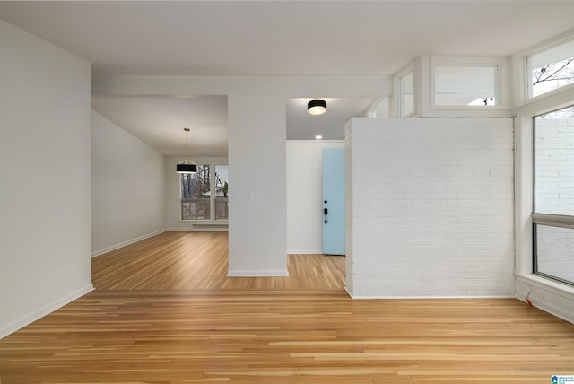 spare room featuring brick wall, a wealth of natural light, and light hardwood / wood-style flooring