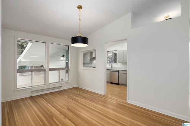 unfurnished dining area featuring light hardwood / wood-style flooring, a baseboard radiator, plenty of natural light, and vaulted ceiling