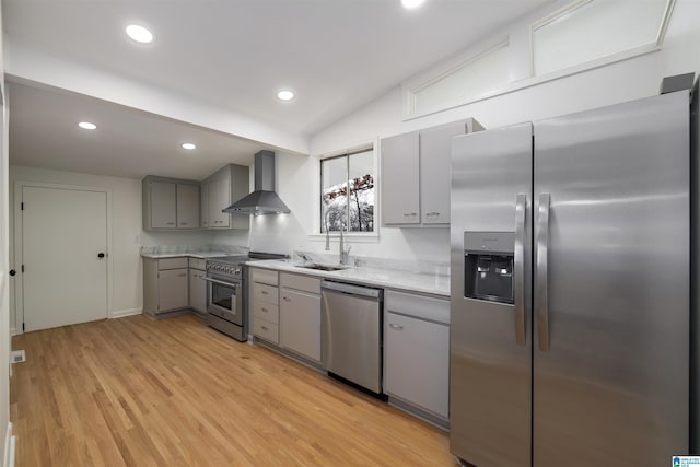 kitchen featuring wall chimney exhaust hood, vaulted ceiling, light hardwood / wood-style flooring, gray cabinets, and stainless steel appliances