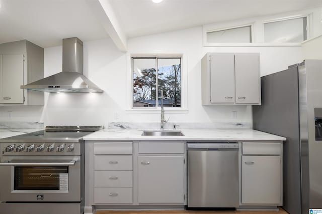 kitchen with lofted ceiling, appliances with stainless steel finishes, sink, and wall chimney range hood