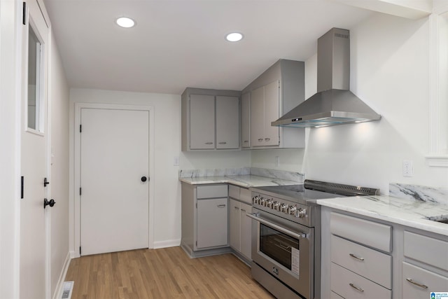 kitchen featuring gray cabinets, high end stainless steel range, light stone countertops, wall chimney range hood, and light hardwood / wood-style flooring