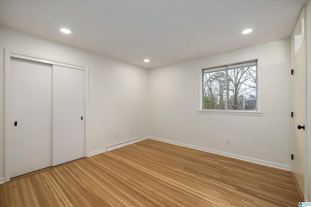 unfurnished bedroom featuring hardwood / wood-style floors, a closet, and baseboard heating