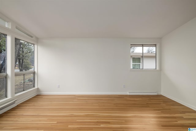 unfurnished room with a baseboard radiator, lofted ceiling, plenty of natural light, and light wood-type flooring