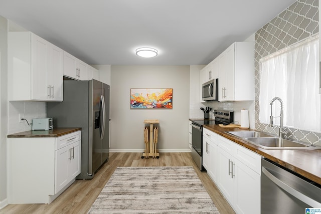 kitchen featuring butcher block countertops, sink, appliances with stainless steel finishes, white cabinetry, and light wood-type flooring