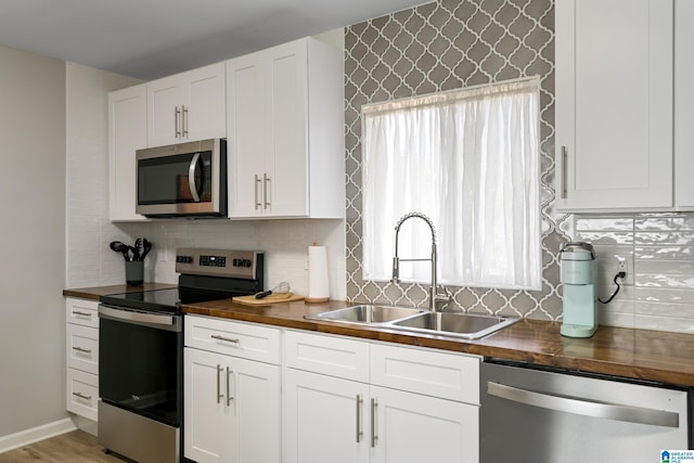 kitchen with sink, appliances with stainless steel finishes, white cabinetry, tasteful backsplash, and wood counters