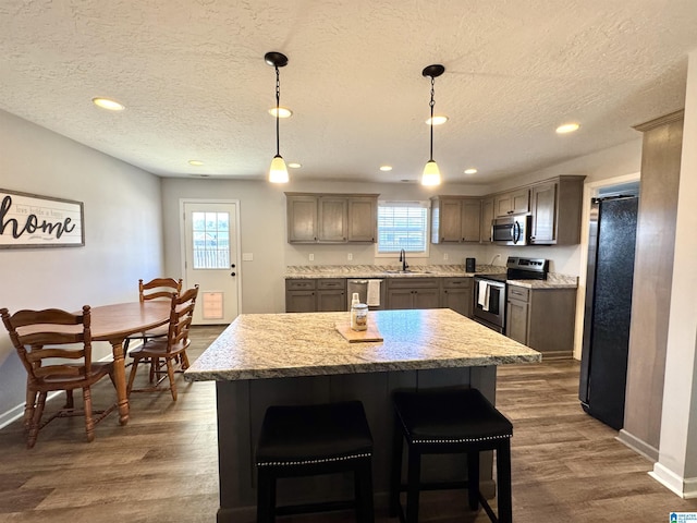 kitchen featuring a kitchen island, dark hardwood / wood-style floors, decorative light fixtures, stainless steel appliances, and a textured ceiling