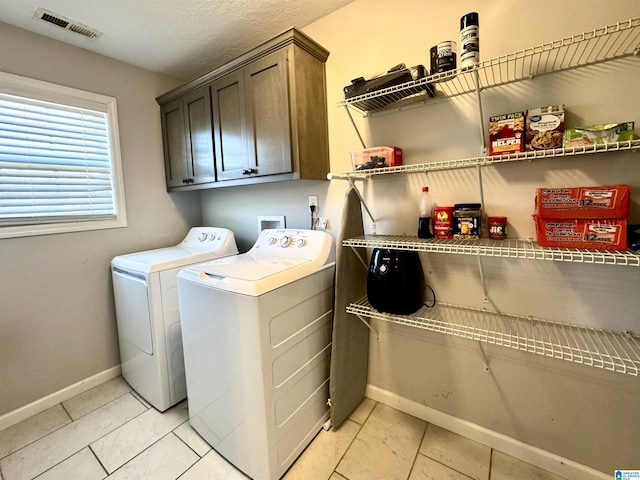 laundry room featuring cabinets, washing machine and clothes dryer, light tile patterned flooring, and a textured ceiling