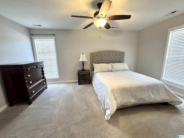 bedroom featuring multiple windows, a textured ceiling, light colored carpet, and ceiling fan