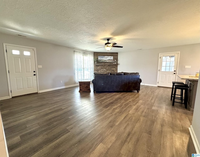 living room with dark wood-type flooring, a healthy amount of sunlight, a stone fireplace, and a textured ceiling