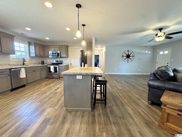 kitchen featuring hardwood / wood-style floors, hanging light fixtures, a center island, stainless steel appliances, and a textured ceiling