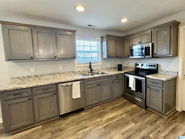 kitchen with sink, dark wood-type flooring, stainless steel appliances, light stone counters, and a textured ceiling