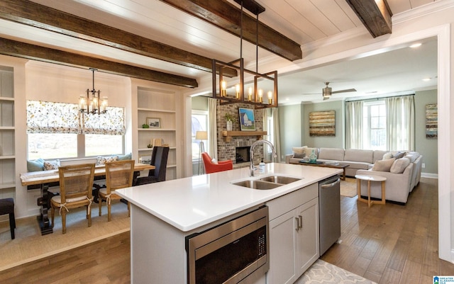 kitchen featuring sink, appliances with stainless steel finishes, a kitchen island with sink, a fireplace, and decorative light fixtures