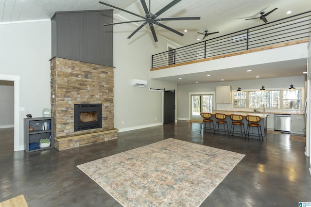 living room with a stone fireplace, a barn door, ceiling fan, and a high ceiling