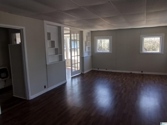 unfurnished room featuring dark wood-type flooring, plenty of natural light, built in features, and a drop ceiling