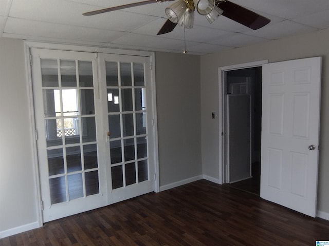 empty room with a drop ceiling, dark hardwood / wood-style flooring, french doors, and ceiling fan