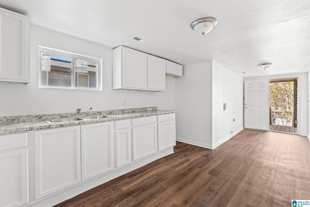 kitchen with white cabinetry, sink, light stone counters, and dark wood-type flooring