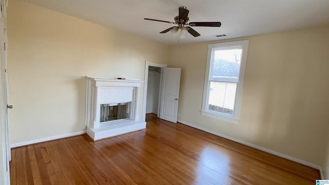 unfurnished living room featuring a brick fireplace, hardwood / wood-style floors, and ceiling fan