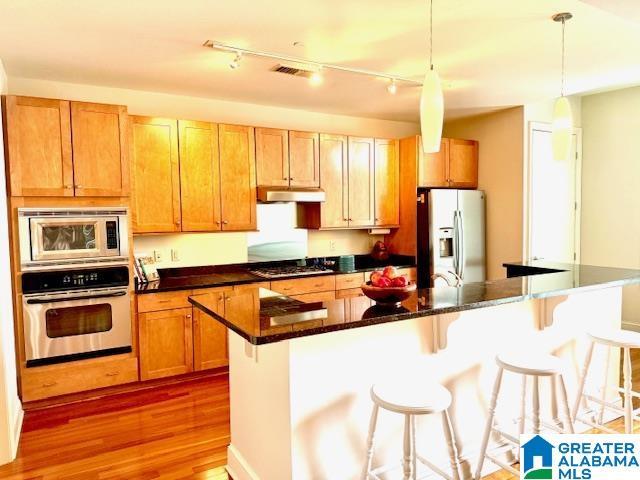 kitchen with a breakfast bar, wood-type flooring, a center island, appliances with stainless steel finishes, and pendant lighting