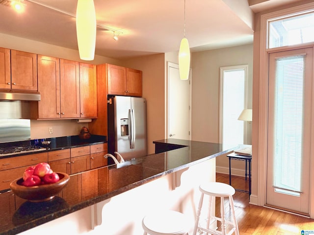 kitchen with stainless steel appliances, a kitchen bar, hanging light fixtures, and dark stone counters