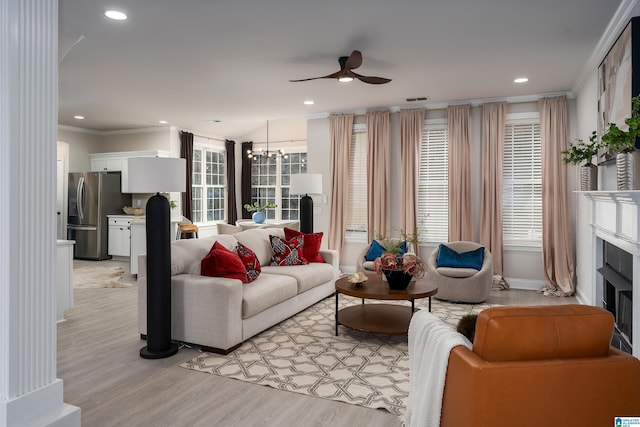 living room with ceiling fan with notable chandelier, ornamental molding, and light hardwood / wood-style floors