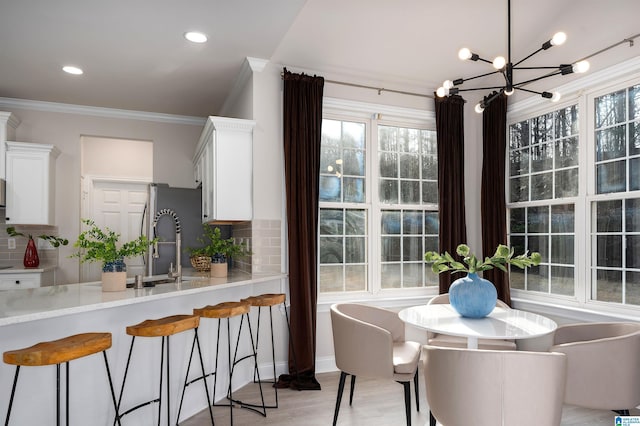 kitchen featuring crown molding, a breakfast bar area, light hardwood / wood-style flooring, white cabinetry, and decorative backsplash