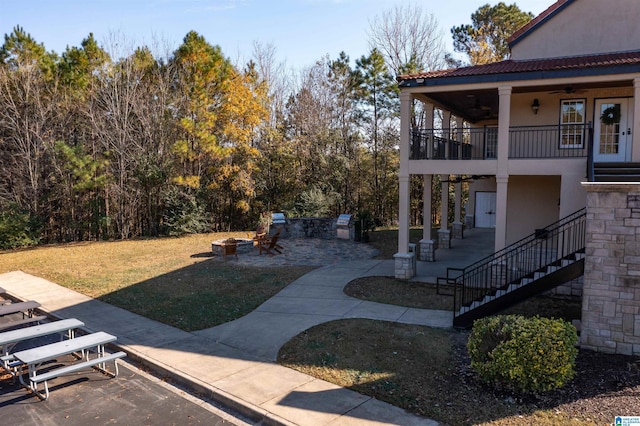 view of yard with ceiling fan, a patio area, a fire pit, and a balcony