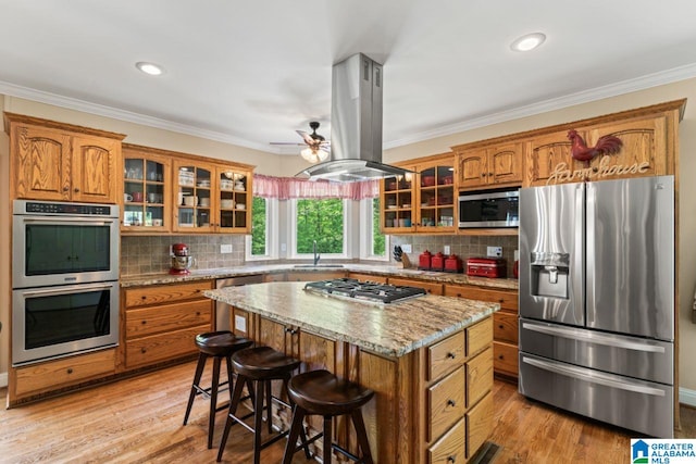 kitchen featuring a kitchen island, island range hood, a breakfast bar area, stainless steel appliances, and crown molding