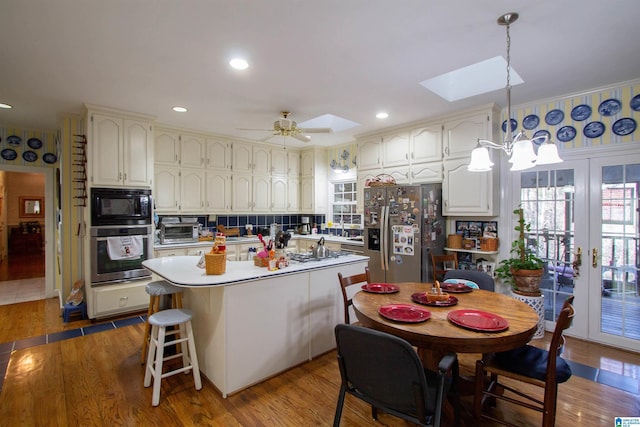 kitchen with a skylight, appliances with stainless steel finishes, a kitchen island, pendant lighting, and hardwood / wood-style floors