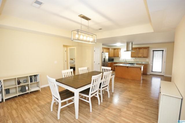 dining room with a tray ceiling, sink, and light hardwood / wood-style flooring