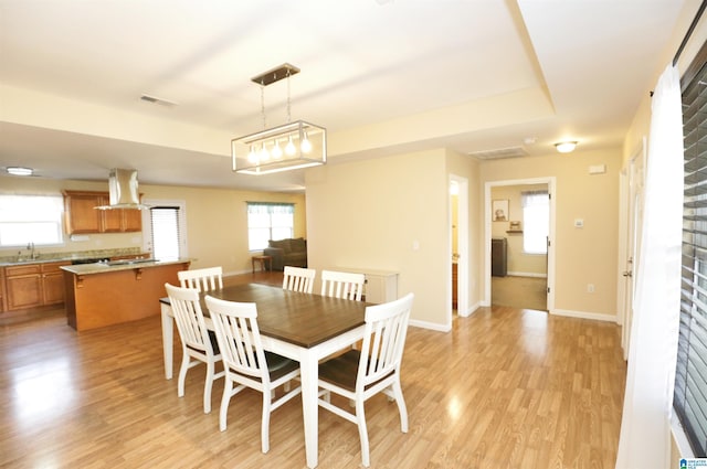 dining area with sink, a tray ceiling, and light wood-type flooring