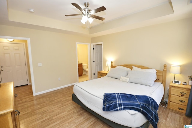 bedroom with ceiling fan, ensuite bath, light hardwood / wood-style floors, and a tray ceiling