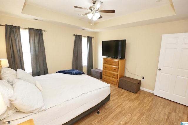 bedroom featuring a raised ceiling, ceiling fan, and light wood-type flooring