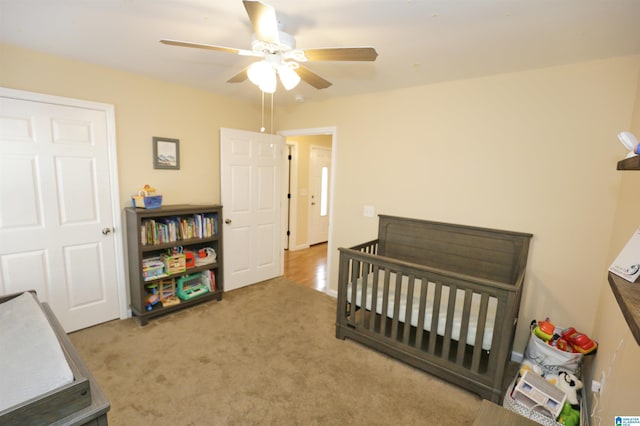 carpeted bedroom featuring a nursery area and ceiling fan