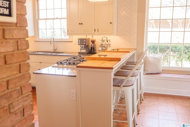 kitchen featuring a breakfast bar, butcher block countertops, tasteful backsplash, sink, and light tile patterned floors