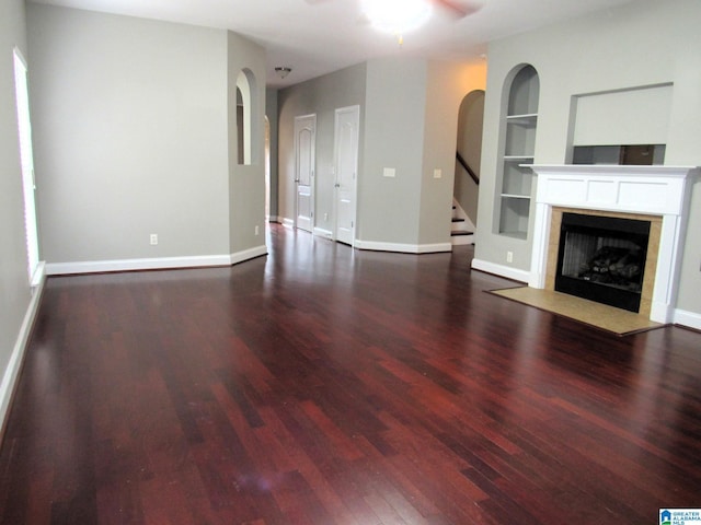 unfurnished living room featuring built in shelves, dark hardwood / wood-style floors, and ceiling fan