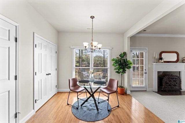 dining space featuring light wood-style flooring, a high end fireplace, visible vents, and an inviting chandelier