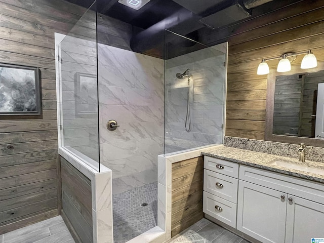 bathroom featuring tiled shower, vanity, and wood walls