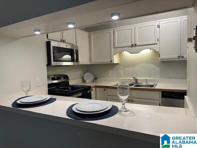 kitchen with stainless steel appliances, white cabinetry, sink, and kitchen peninsula