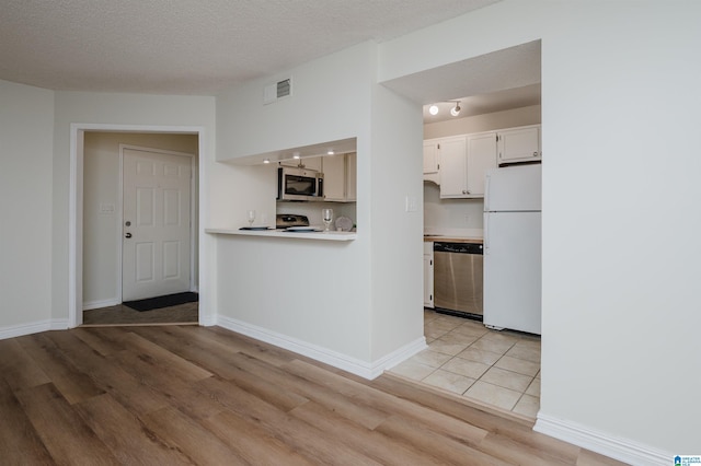 kitchen with white cabinetry, stainless steel appliances, a textured ceiling, and light wood-type flooring